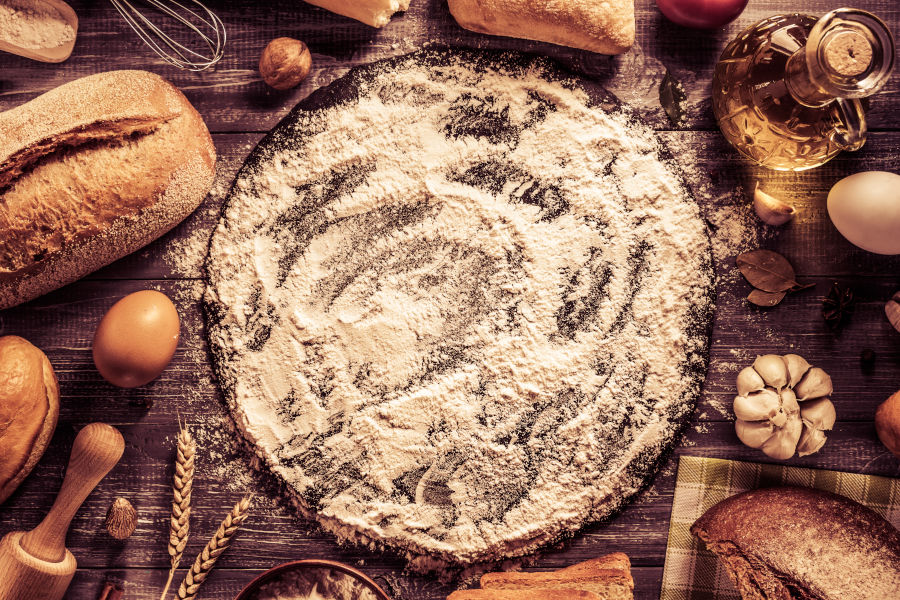 Regionale Produkte Mehl, Brot, Eier, Knoblauch und Öl auf einem rustikalen Holztisch angerichtet.